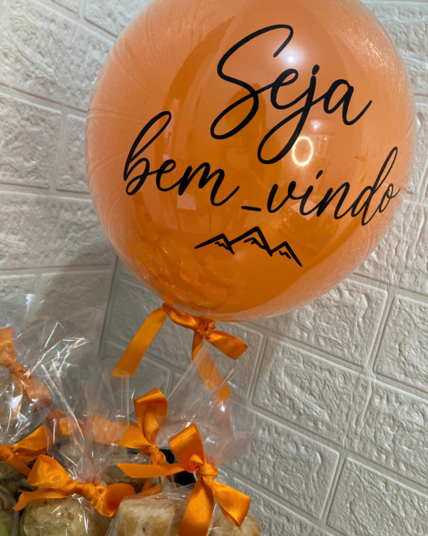 Cesta Box Legendário 3 Balão laranja flutuante com a mensagem Seja bem_vindo e ícone de montanhas, amarrado à Box Legendário recheada de pães e biscoitos.