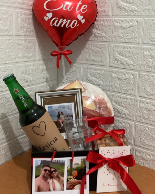 Box Happy Hour a Dois em caixa preta com balão de coração vermelho. Contém cerveja Heineken, dois copos Lagoinha, moldura com foto, tábua de charcutaria, amendoins e fotografias polaroid.
