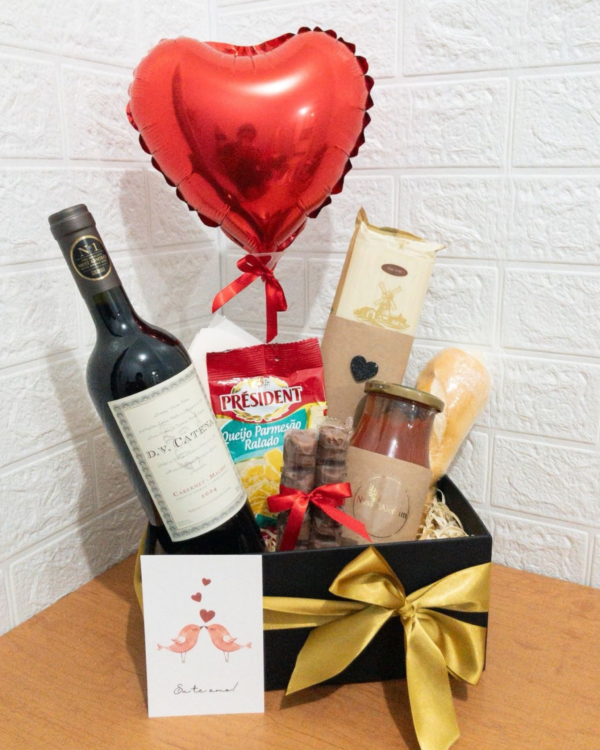 Box Jantar a Dois em caixa preta com laço dourado. Contém vinho D.V. Catena, queijo ralado Président, molho de tomate, macarrão, Kinder Bueno, balão de coração vermelho e cartão Eu te amo.