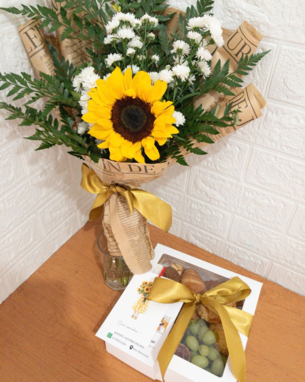 Cesta Café Mimo 2 Cesta Café Mimo da Nosso Alecrim em caixa branca com visor e laço dourado, acompanhada de um lindo buquê de girassol e flores brancas rústico, sobre mesa de madeira.