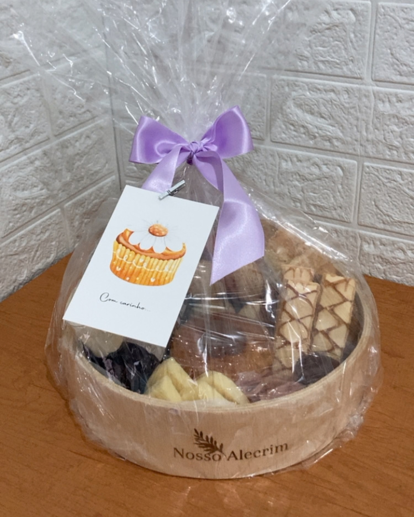 Cesta P embalada para presente com celofane transparente, laço de fita lilás e cartão com ilustração de cupcake escrito Com carinho