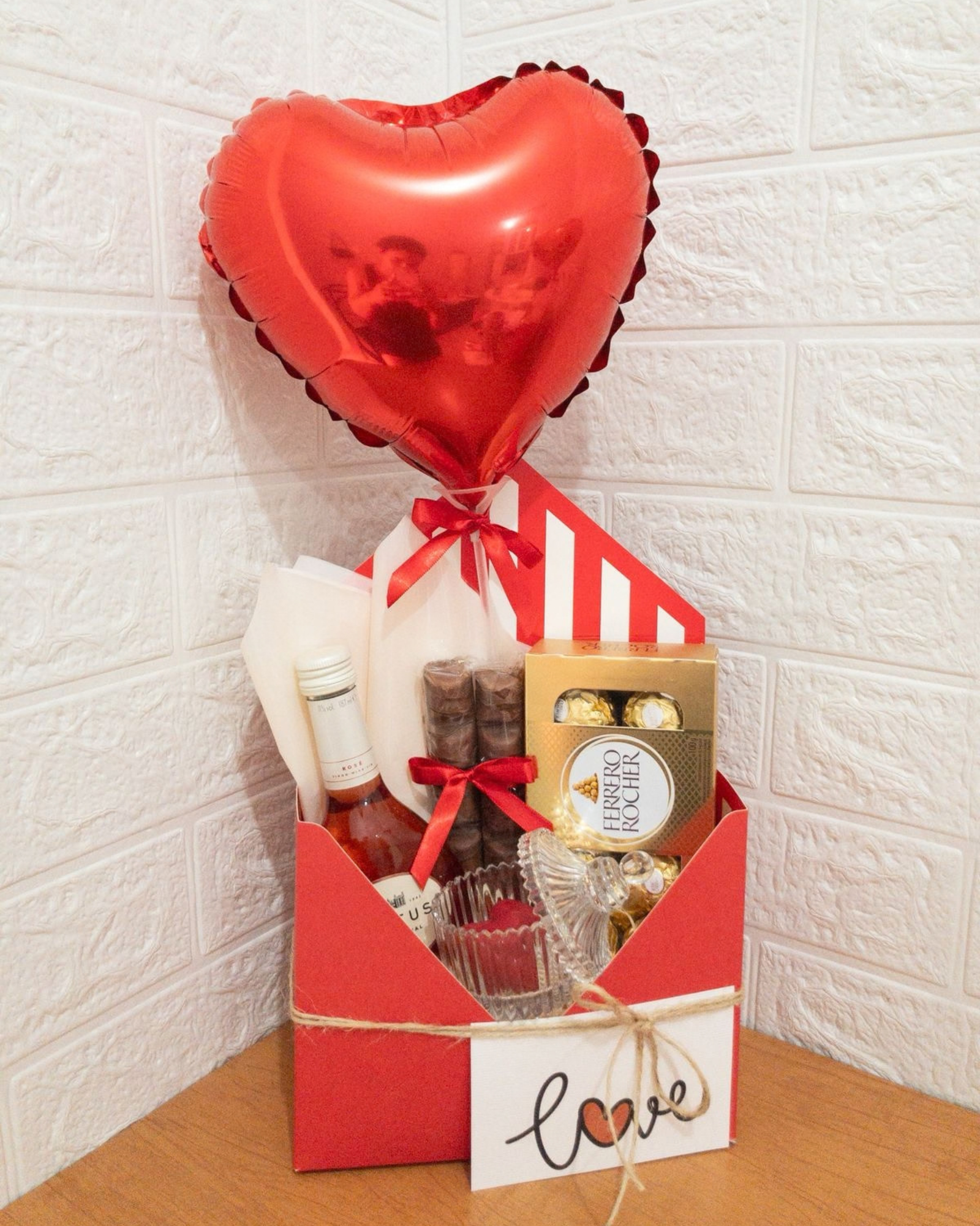 Cesta de Vinho e Chocolate 1 Cesta romântica em caixa envelope com vinho rosé, chocolates Ferrero Rocher e balão de coração.