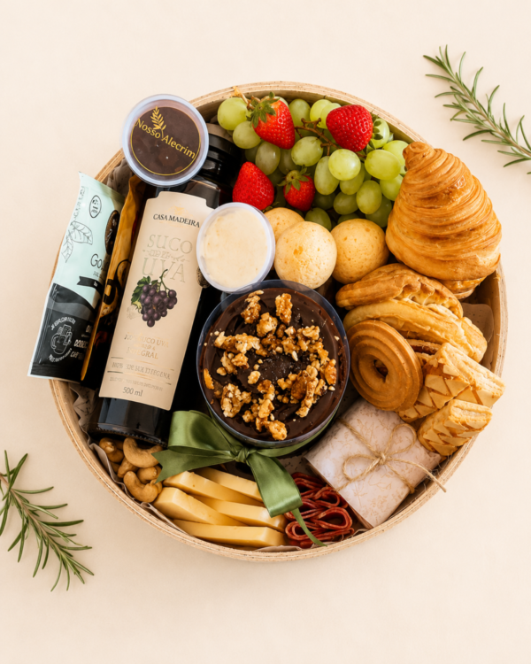 Close-up na Cesta Café Celebrar destacando o bolo bentô de chocolate com nozes, o rótulo do suco de uva Casa Madeira, potes de geleia, biscoitos finos e frutas frescas.