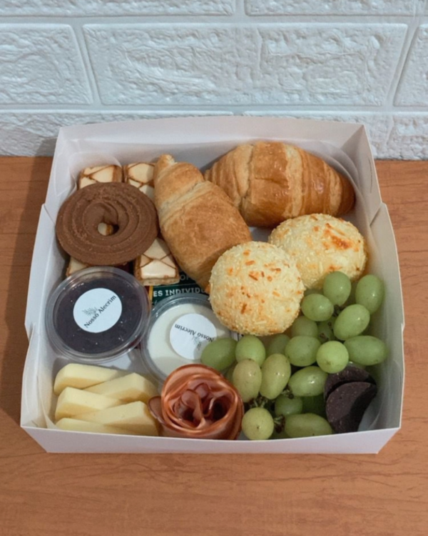 Cesta Café Mimo 5 Visão interna da Cesta Café Mimo mostrando croissants, grandes pães de queijo, biscoitos finos, uvas verdes, charcutaria em formato de rosa, fatias de queijo e potinhos de geleia e cream cheese.